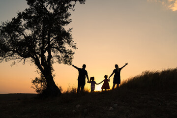 Happy family silhouette standing on against beautidul sunset view.