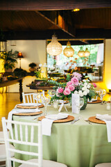 Wedding table with white chairs, white plates, and a floral arrangement featuring roses. A romantic and elegant setup for a wedding reception, blending simplicity, beauty, and natural charm.