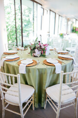 Wedding table with white chairs, white plates, and a floral arrangement featuring roses. A romantic and elegant setup for a wedding reception, blending simplicity, beauty, and natural charm.