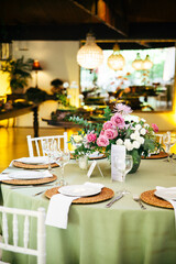 Wedding table with white chairs, white plates, and a floral arrangement featuring roses. A romantic and elegant setup for a wedding reception, blending simplicity, beauty, and natural charm.