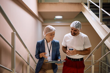 Happy quality control manager and worker analyzing reposts in a hallway.