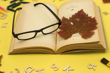 Autumn dried maple leaf, open book and reading glasses. Nostalgia. Autumn background