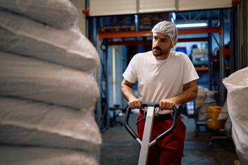Factory worker using pallet jack in a storage room.