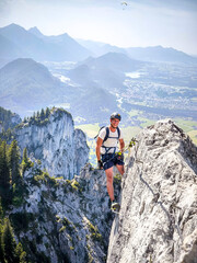 Climber On Fingersteig Via Ferrata Near Tegelberg: Adventurer Traversing Narrow Ridge With Harness And Helmet Against A Stunning Alpine Backdrop In Bavaria, Germany