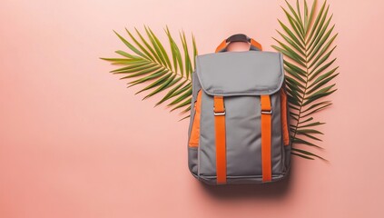 Photo of a gray backpack with orange straps and one small palm leaf on the top, against a pastel peach background. Web banner with copy space on the left side