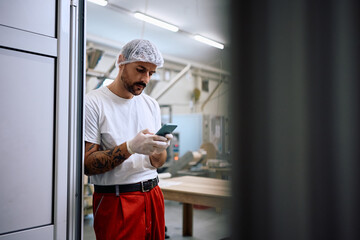 Production facility worker text messaging on cell phone during his break at work.