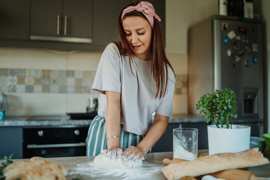 Young caucasian woman making bread dough with rolling pin and flour