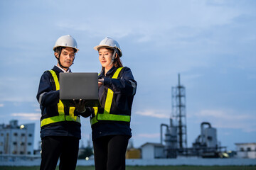 Two industrial engineers—a man and a woman—wearing safety helmets and reflective vests are...
