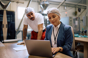 Female manager working on laptop while supervising production in a factory.