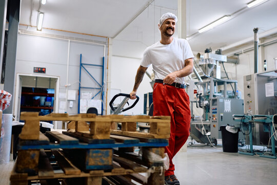Happy worker pulling pallet jack while working at food factory.
