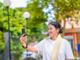 Happy senior woman enjoying using smartphone for video call, research browser, chat communication or calling to family after exercise in park holiday. Elderly use technology in lifestyle. Healthcare 