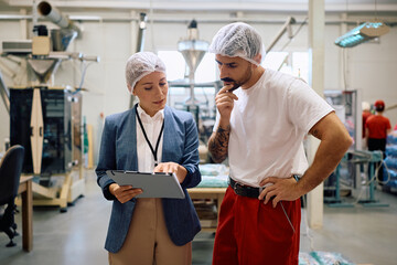 Naklejka na ściany i meble Female manager and employee going through paperwork at factory plant.