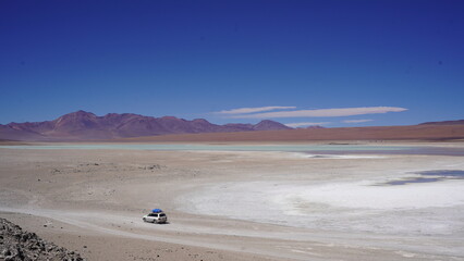 Colorful Bolivian lagoon surrounded by dramatic mountains, salt flats, flamingos, and off-road explorers in the remote altiplano
