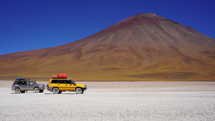 Colorful Bolivian lagoon surrounded by dramatic mountains, salt flats, flamingos, and off-road explorers in the remote altiplano