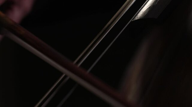 An elegant close-up of a cellist's hand bowing strings. The shot shifts to the bridge, showing detailed, skilled technique during a classical music performance with beautiful bokeh.