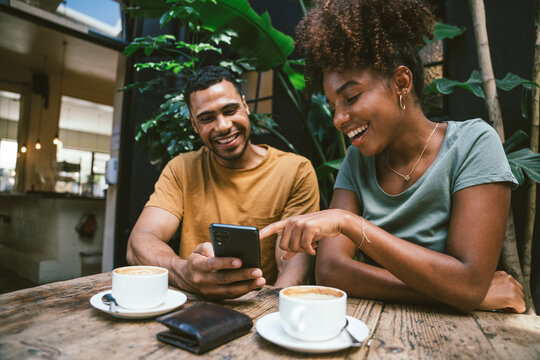 Smiling couple using smartphone at wooden table in coffee shop
