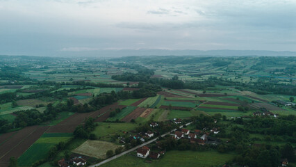 Aerial view of green rural landscape with red-roof houses surrounded by fields and orchards in Serbia at sunset