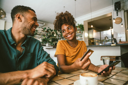 Smiling couple making payment using smartphone and credit card at cafe table