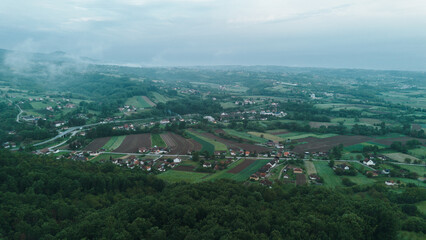 Aerial view of green rural landscape with red-roof houses surrounded by fields and orchards in...