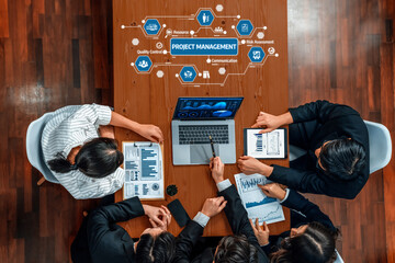 A top-down view of a project management meeting with a team discussing data and strategies. The...