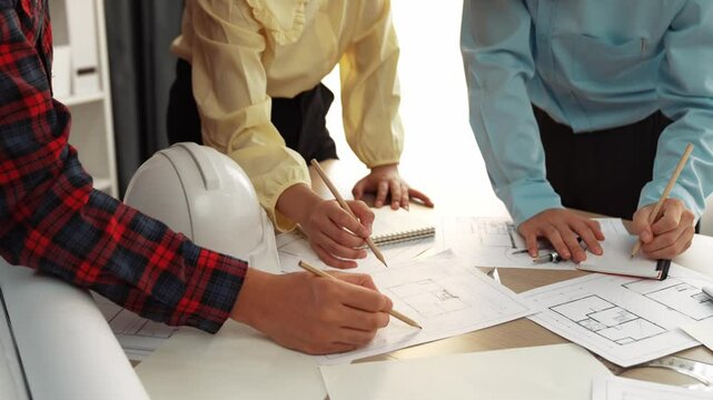 Smart architect and safety engineer discussion about building blueprint on table with architectural document, measurement tools and wooden block scatter around at modern office. Closeup. Delineation.