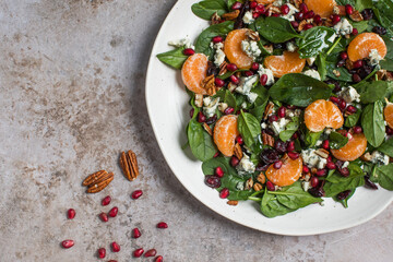 An appetizing festive salad of fresh spinach, tangerine, pomegranate and pine nuts on a plate. Copy...