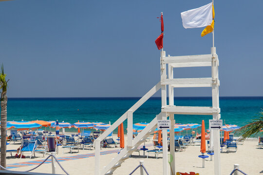 Lifeguard tower on a sandy beach with colorful umbrellas and clear blue sea.Mediterranean Sea. Colorful umbrellas and sun loungers against the backdrop of a crystal clear turquoise sea. - Powered by Adobe