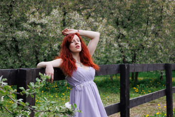 red-haired girl with curly hair walks in the park. Girl in a smart dress smiles. Woman poses...