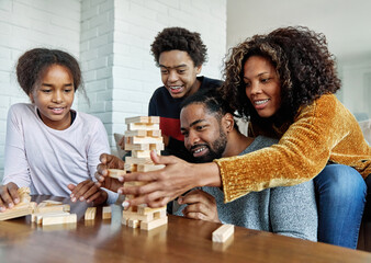Portrait of a happy african american family at home, having fun playing wooden brick challenge game, playing board game jenga at home