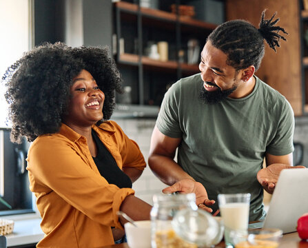 Happy young afro american couple having fun preparing food and looking for recipes online using a laptop in kitchen