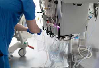 Nurse connecting a transparent bag to a dialysis machine in a hospital room