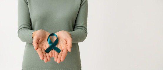 Woman holding teal awareness ribbon in hands on white background with copy space. Concept of ovarian cancer support, sexual assault prevention, PCOS awareness, PTSD and mental health, wide banner