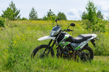 Off-road enduro motorcycle stands next to a country road in the middle of a field in tall grass