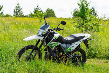 Off-road enduro motorcycle stands next to a country road in the middle of a field in tall grass