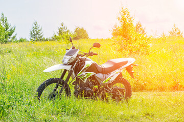 Off-road enduro motorcycle stands next to a country road in the middle of a field in tall grass