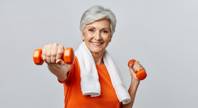 Smiling senior woman with gray hair exercising with orange dumbbells and a towel. Represents active aging, fitness, and a healthy lifestyle.