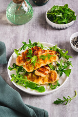 Crispy fried halloumi cheese and arugula leaves on a plate on a table vertical view