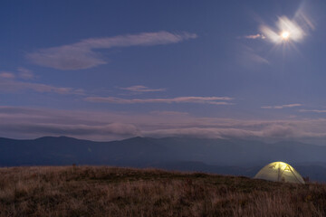 Beautiful mountain landscape. Tourist tent against the backdrop of mountains. Light in the tent that stands on the top of the mountain.