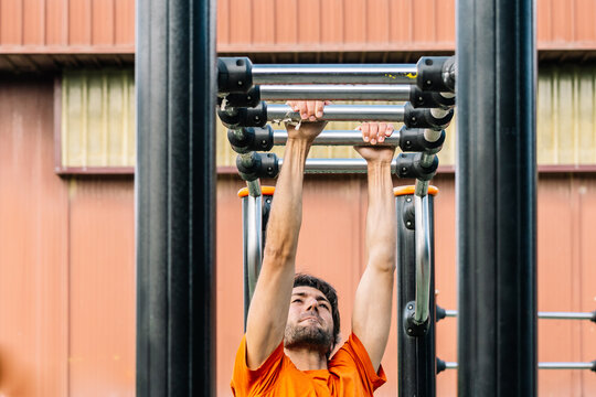 Determined athlete performing pull-ups on outdoor gym equipment for upper body strength training - Powered by Adobe