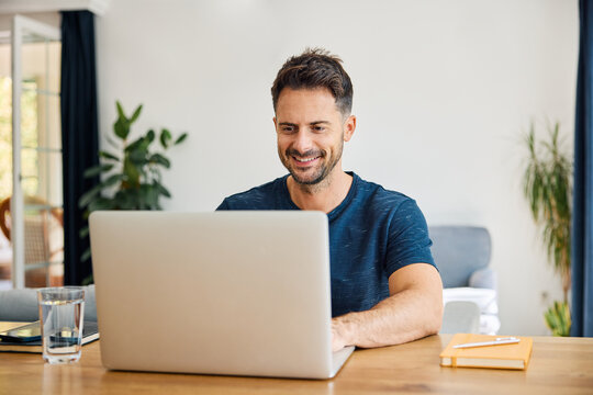 Smiling man sitting at desk with laptop at home