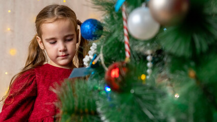 Little girl wearing red christmas dress and to decorate Christmas Tree at home