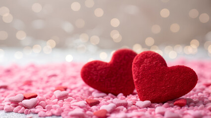 Obraz premium Two red hearts sit among pink heart shaped candy sprinkles with bokeh background