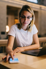 Smart female student synchronizing netbook files with smartphone doing homework in library,hipster...