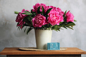 Pink peonies in a metal vase and wooden calendar showing july 23rd, date concept