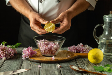 A chef skillfully squeezes a fresh lemon over a bowl filled with vibrant edible flower petals. The rustic kitchen showcases natural light and wooden surfaces, enhancing the culinary atmosphere
