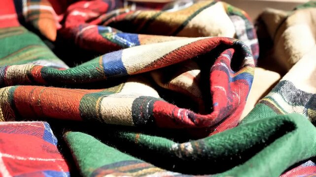 Close-up of folded checkered flannel fabric in shades of red, green, beige, brown, and blue with intricate patterns and soft textures