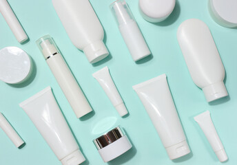 A variety of white plastic tubes and bottles with cosmetics, randomly arranged on a light blue...