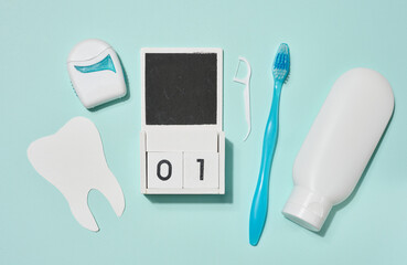 Blue toothbrush, white tube of toothpaste, dental floss in blue case and wooden calendar, paper...