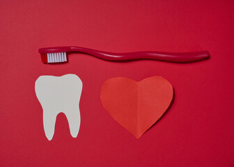 Red toothbrush, white paper tooth cut out and red paper heart placed on red background.