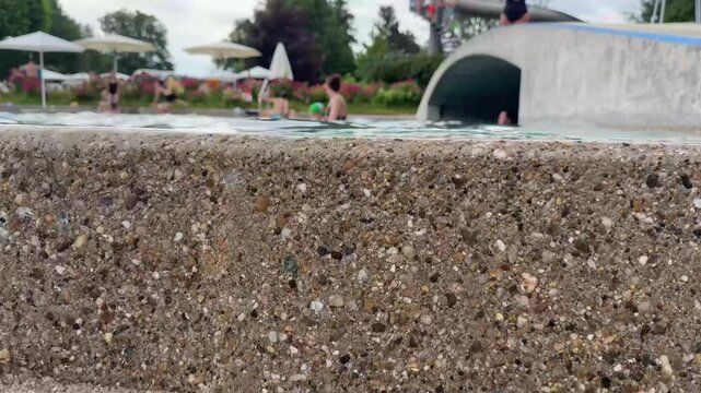 Water overflowing from pool edge with textured stone surface, public swimming pool in summer, ecosystem and water usage concept (Slow motion)